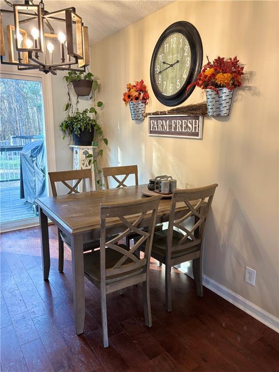 dining area with a textured ceiling, hardwood / wood-style floors, baseboards, and a notable chandelier