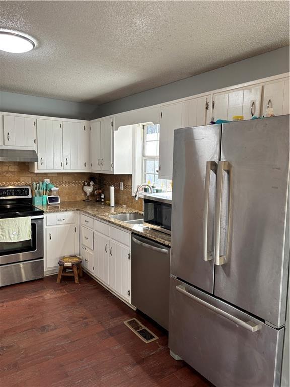 kitchen with under cabinet range hood, stainless steel appliances, dark wood-style flooring, visible vents, and white cabinets