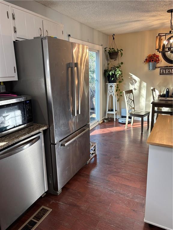 kitchen featuring dark wood finished floors, stainless steel appliances, white cabinetry, a textured ceiling, and a chandelier