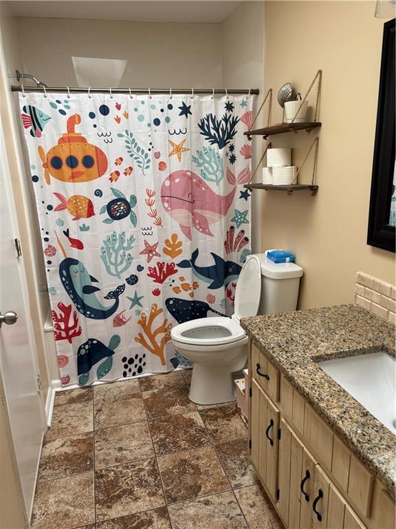 bathroom featuring stone finish floor, a shower with shower curtain, vanity, and toilet