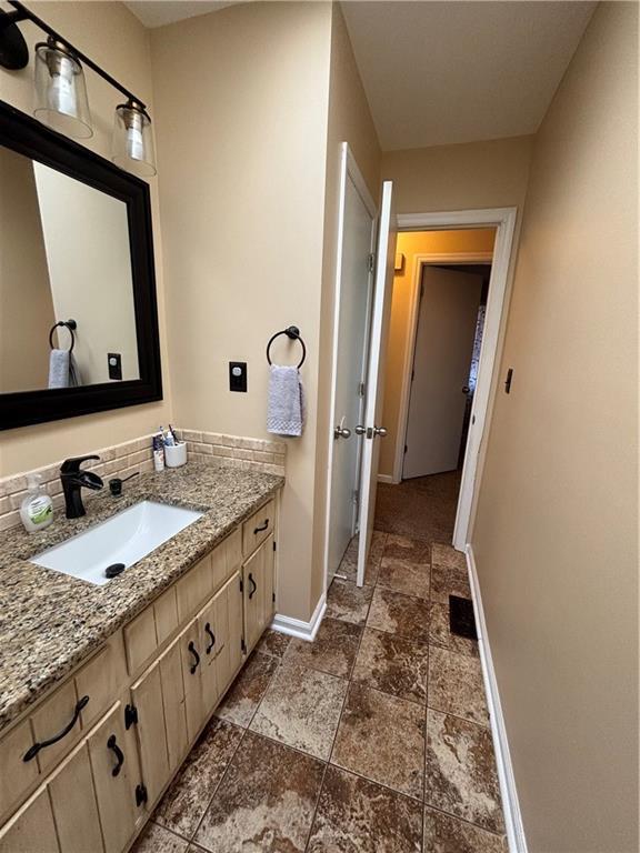 bathroom with stone finish flooring, tasteful backsplash, vanity, and baseboards