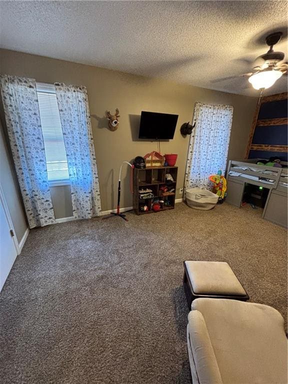 living area with ceiling fan, a textured ceiling, carpet, and baseboards