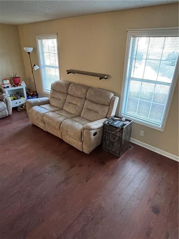 living area featuring a textured ceiling, dark wood finished floors, and baseboards