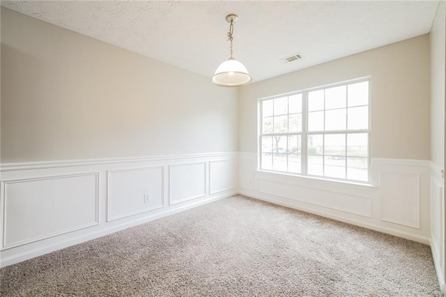 carpeted spare room featuring a textured ceiling, wainscoting, and visible vents