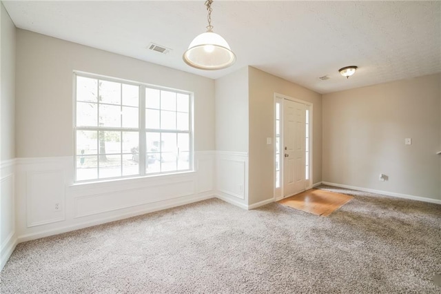 foyer entrance with wainscoting, visible vents, a decorative wall, and light carpet