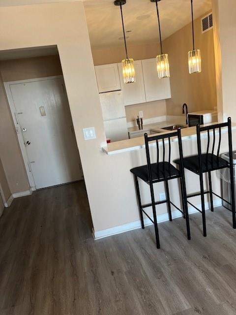 kitchen with sink, dark hardwood / wood-style floors, white cabinets, a kitchen bar, and decorative light fixtures