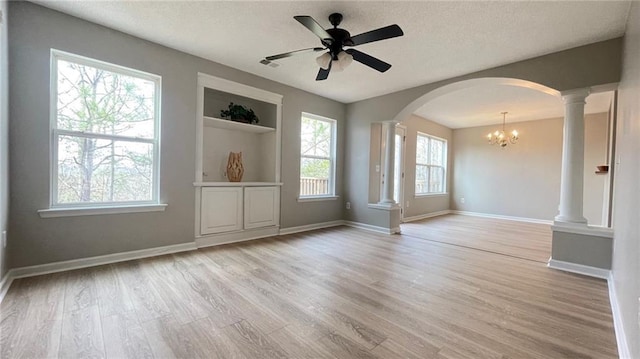 empty room featuring decorative columns, light hardwood / wood-style floors, built in shelves, a textured ceiling, and ceiling fan with notable chandelier