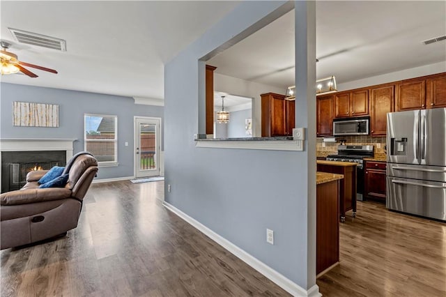 kitchen featuring appliances with stainless steel finishes, ceiling fan, dark wood-style flooring, decorative backsplash, and baseboards