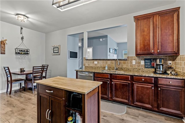 kitchen with a sink, stainless steel dishwasher, light wood-style flooring, and decorative backsplash