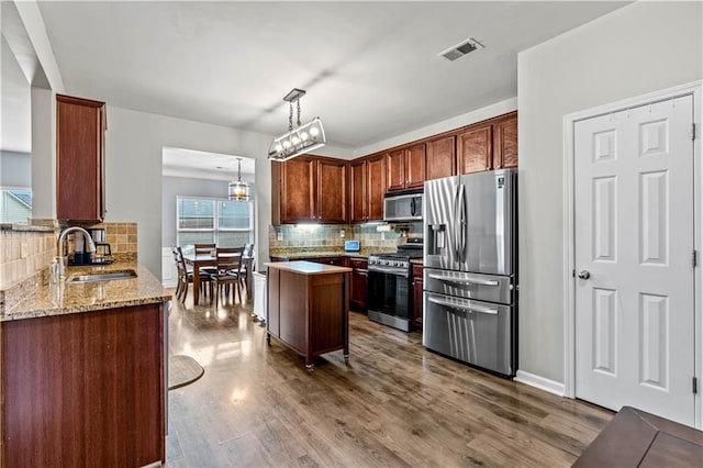 kitchen with appliances with stainless steel finishes, a sink, backsplash, and light stone counters