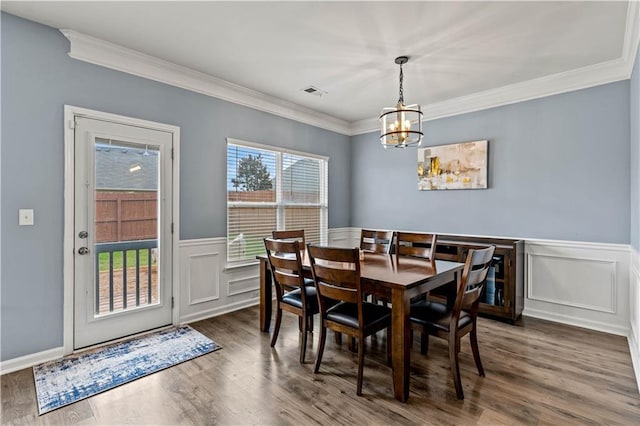 dining space featuring a chandelier, ornamental molding, wainscoting, wood finished floors, and a decorative wall