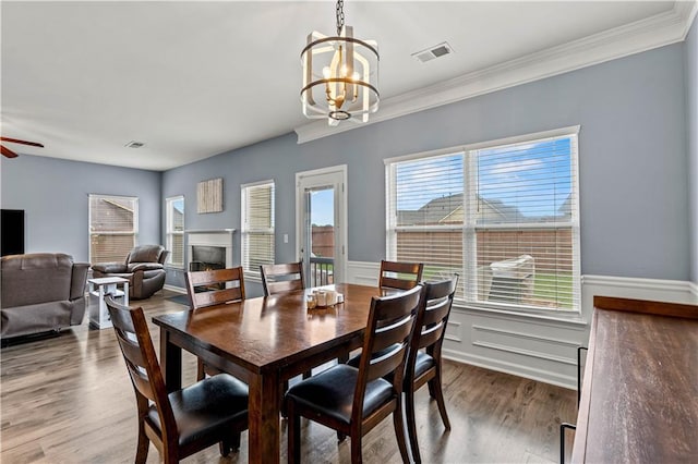 dining room with a chandelier, a lit fireplace, wood finished floors, ceiling fan, and wainscoting