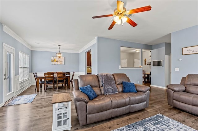 living area featuring ceiling fan, a chandelier, baseboards, wood finished floors, and crown molding