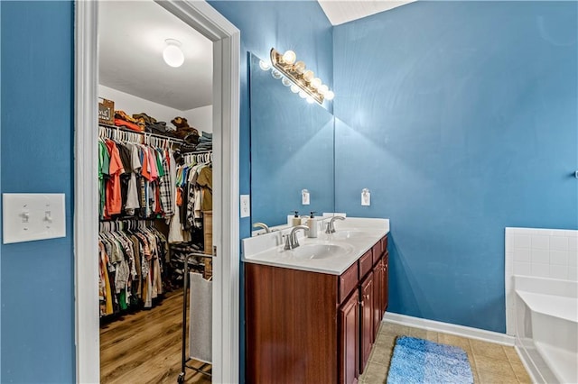 bathroom featuring a spacious closet, a garden tub, double vanity, and baseboards