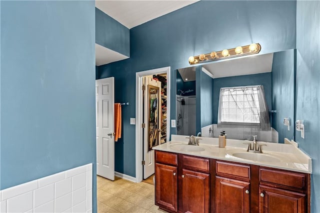 full bath with double vanity, a shower, and a walk in closet