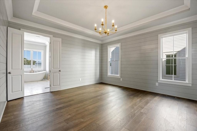 empty room featuring a tray ceiling, dark hardwood / wood-style floors, and a notable chandelier