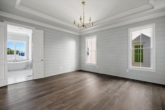 empty room featuring dark wood-type flooring, a tray ceiling, and a notable chandelier