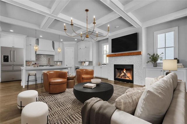 kitchen with premium range hood, white cabinets, a kitchen island with sink, beamed ceiling, and hanging light fixtures