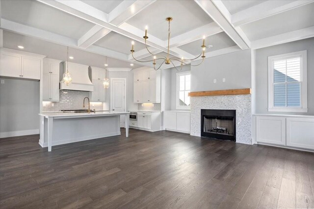 kitchen with white cabinets, decorative light fixtures, custom range hood, and a kitchen island with sink