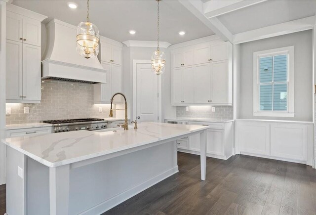 kitchen with custom exhaust hood, white cabinetry, a kitchen island with sink, and hanging light fixtures