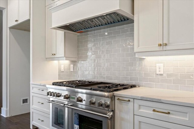 kitchen with light stone countertops, dark wood-type flooring, tasteful backsplash, premium range hood, and double oven range