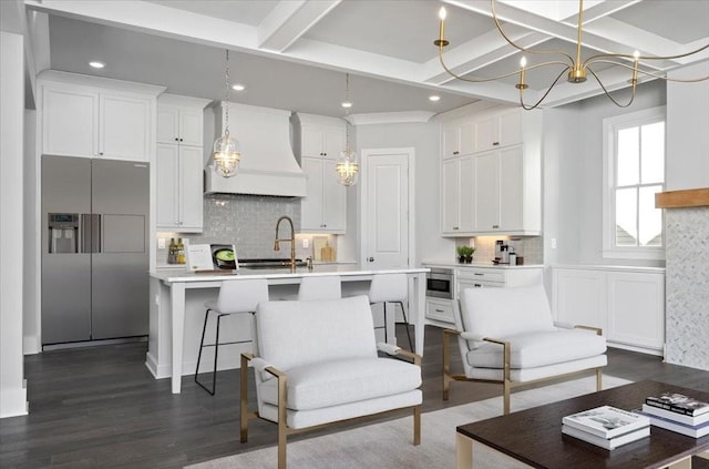 kitchen with custom range hood, a kitchen island with sink, beam ceiling, stainless steel fridge with ice dispenser, and white cabinetry