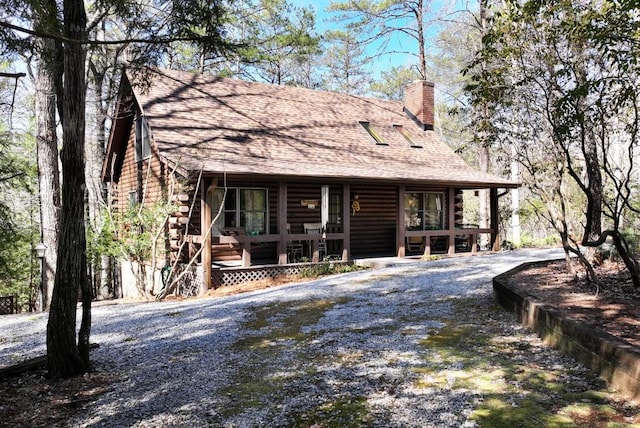 view of front of property featuring gravel driveway, covered porch, a shingled roof, and log exterior