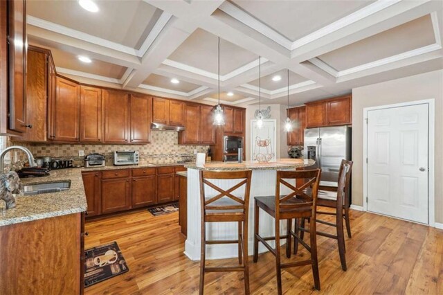 1249 Austin Thomas Dr, Dacula, GA 30019 - kitchen featuring light stone countertops, a kitchen bar, under cabinet range hood, a sink, and light wood-style flooring
