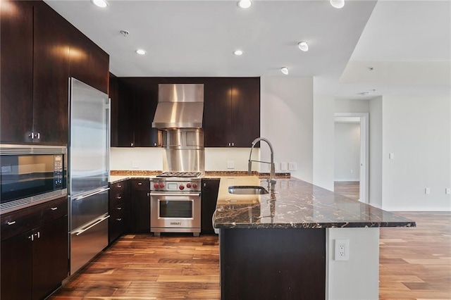 kitchen with built in appliances, light hardwood / wood-style floors, wall chimney range hood, and sink