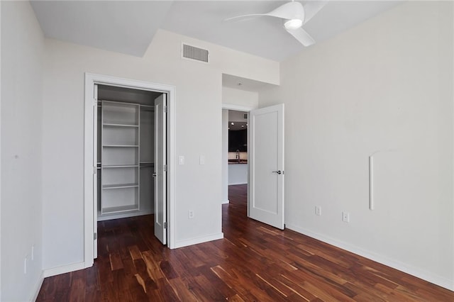 unfurnished bedroom with a closet, a spacious closet, ceiling fan, and dark wood-type flooring