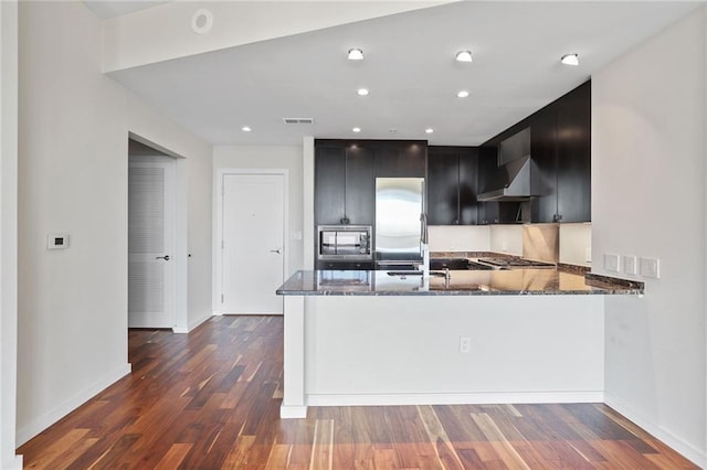 kitchen with wall chimney exhaust hood, dark hardwood / wood-style floors, stone countertops, and kitchen peninsula