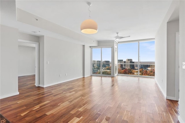 spare room featuring wood-type flooring, a wall of windows, and ceiling fan