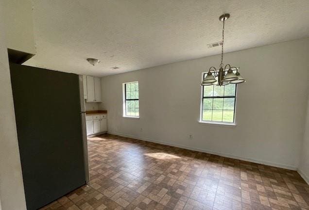 unfurnished dining area with a textured ceiling, plenty of natural light, and a chandelier