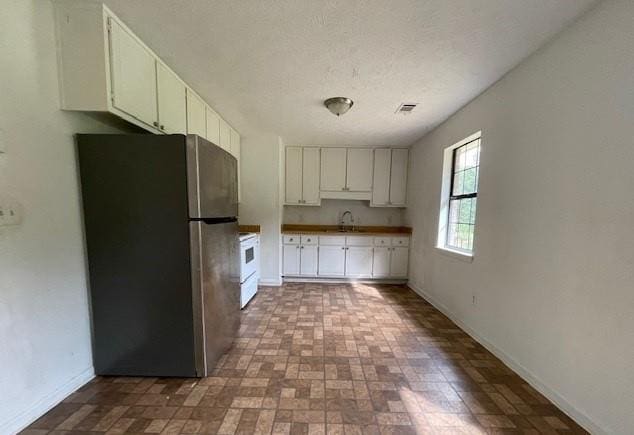 kitchen with white cabinets, stainless steel fridge, sink, a textured ceiling, and electric range