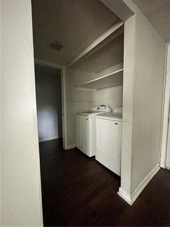 clothes washing area with a textured ceiling, dark wood-type flooring, and washer and clothes dryer