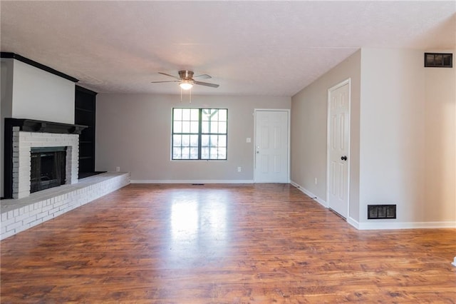 unfurnished living room with ceiling fan, visible vents, a fireplace, and wood finished floors