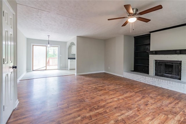 unfurnished living room with a brick fireplace, built in shelves, a textured ceiling, and wood finished floors