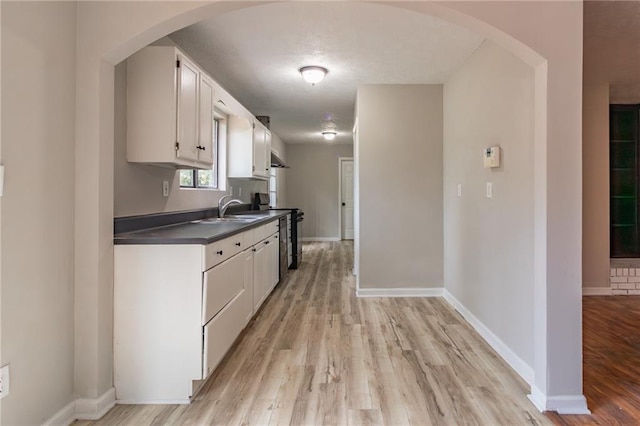 kitchen with light wood-style floors, arched walkways, electric range, and dark countertops