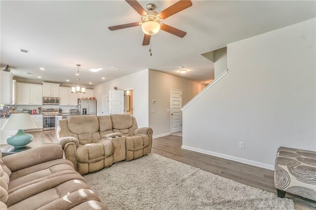 living room with ceiling fan with notable chandelier and light hardwood / wood-style flooring