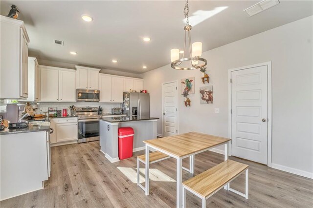 kitchen featuring appliances with stainless steel finishes, tasteful backsplash, decorative light fixtures, a center island, and light hardwood / wood-style floors