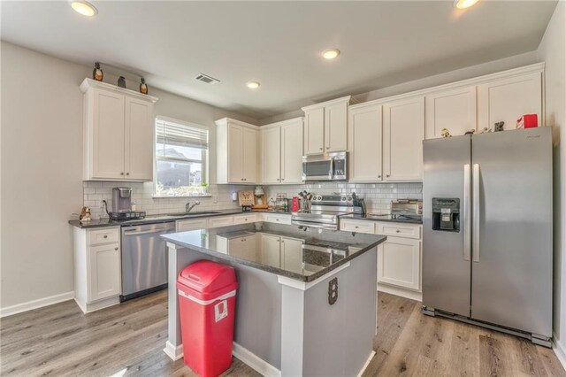 kitchen with a kitchen island, light wood-type flooring, appliances with stainless steel finishes, and tasteful backsplash