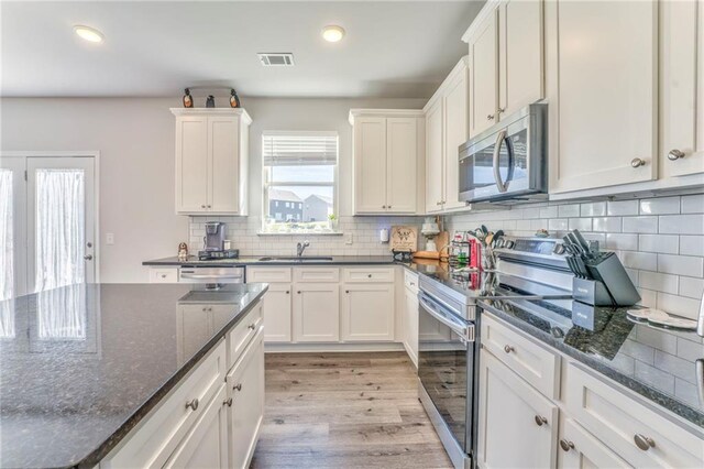 kitchen featuring backsplash, light hardwood / wood-style flooring, dark stone countertops, appliances with stainless steel finishes, and white cabinetry