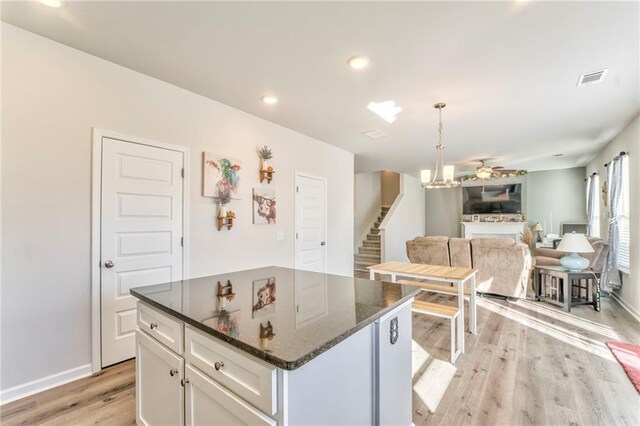 kitchen with pendant lighting, dark stone countertops, white cabinetry, and light hardwood / wood-style flooring