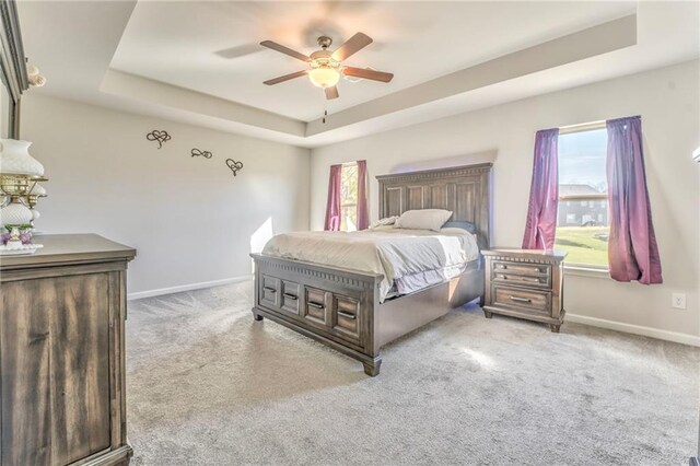 bedroom with ceiling fan, light carpet, and a tray ceiling