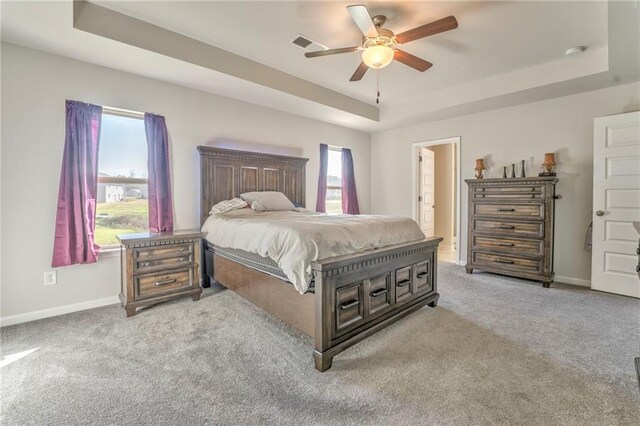 carpeted bedroom featuring a tray ceiling, connected bathroom, and ceiling fan