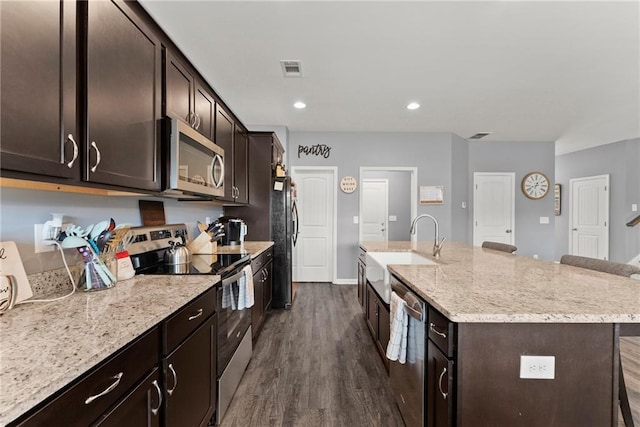 kitchen featuring visible vents, appliances with stainless steel finishes, a center island with sink, a sink, and dark wood-style floors
