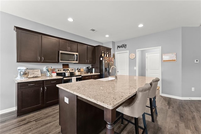 kitchen with dark wood-style flooring, appliances with stainless steel finishes, an island with sink, baseboards, and visible vents