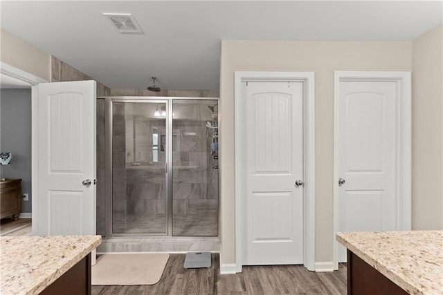 bathroom featuring visible vents, vanity, wood finished floors, baseboards, and a stall shower