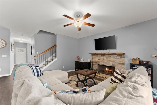 living area featuring ceiling fan, a stone fireplace, wood finished floors, baseboards, and stairs