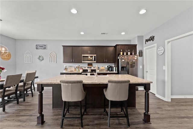 kitchen featuring visible vents, dark wood-style flooring, dark brown cabinets, a breakfast bar area, and stainless steel appliances